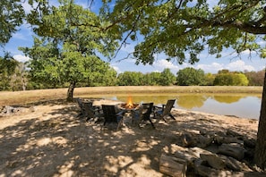 A campsite with a fire pit surrounded by chairs, a pond, and trees.