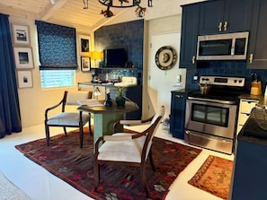 A modern kitchen with dark blue cabinets, a stainless steel stove, and a microwave. There is a dining area with two chairs and a table.