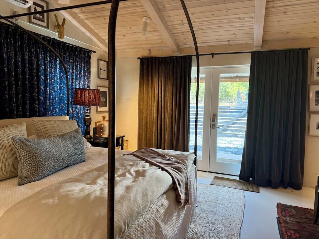 Ein Schlafzimmer mit Bett, Nachttisch, Lampe und Blick ins Freie durch eine Tür.