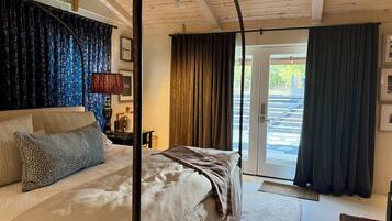 Ein Schlafzimmer mit Bett, Nachttisch, Lampe und Blick ins Freie durch eine Tür.