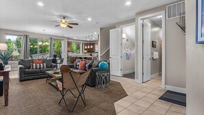 A spacious living room with a sofa, coffee table, and a ceiling fan. There is a kitchen area with cabinets and a dining table. The room has large windows and a view of greenery outside. - Entrada at Moab 624 and 632 (Moab)
