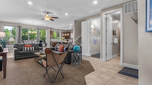 A spacious living room with a sofa, coffee table, and a ceiling fan. There is a kitchen area with cabinets and a dining table. The room has large windows and a view of greenery outside. - Entrada at Moab 624 and 632 (Moab)
