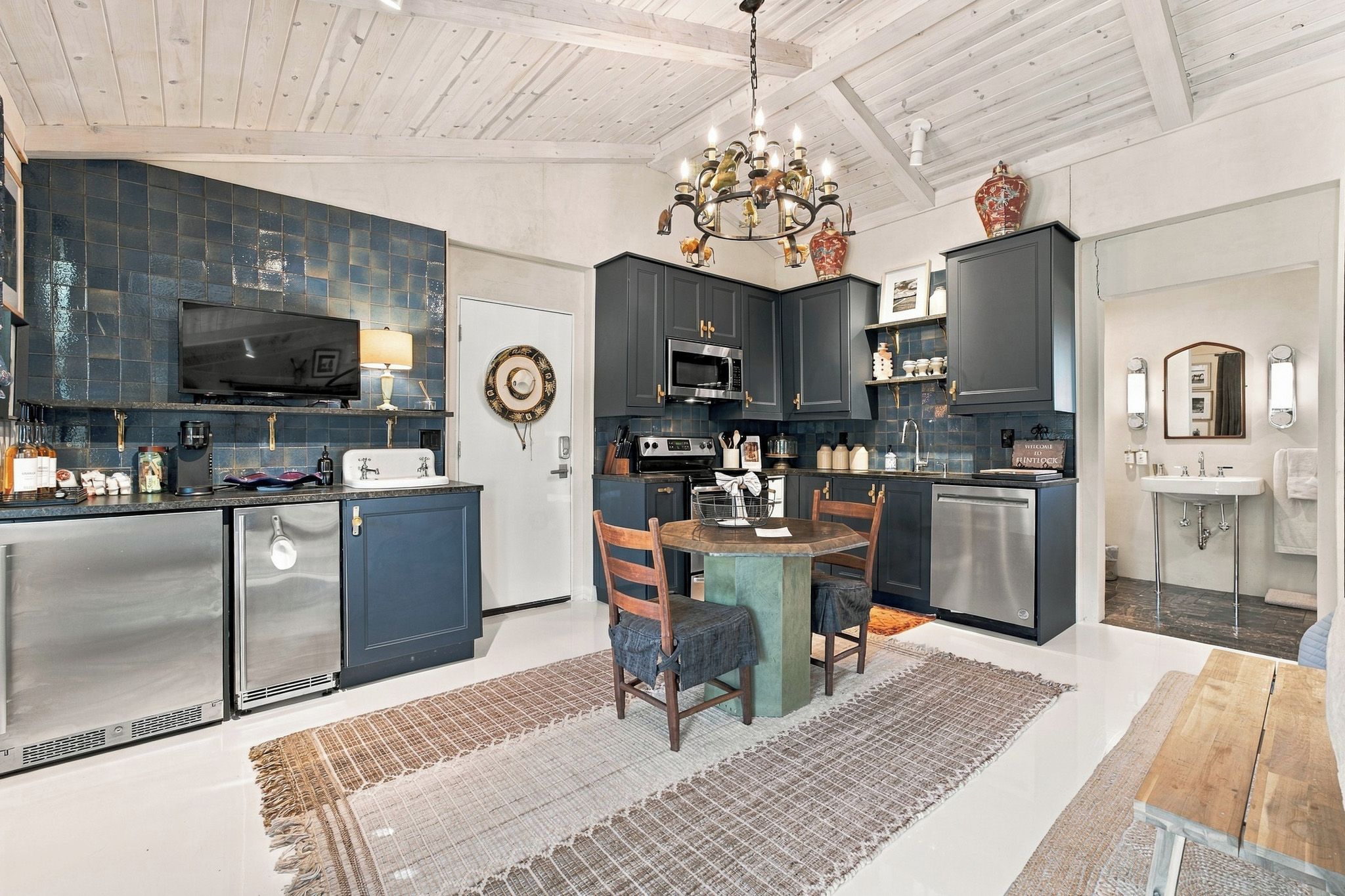 A modern kitchen with dark cabinetry, a dining area with a wooden table and chairs, and a chandelier.