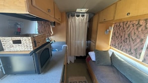 A compact RV interior with a kitchenette, a small seating area, and a shower stall.