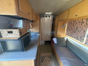 A compact RV interior with a kitchenette, a small seating area, and a shower stall.