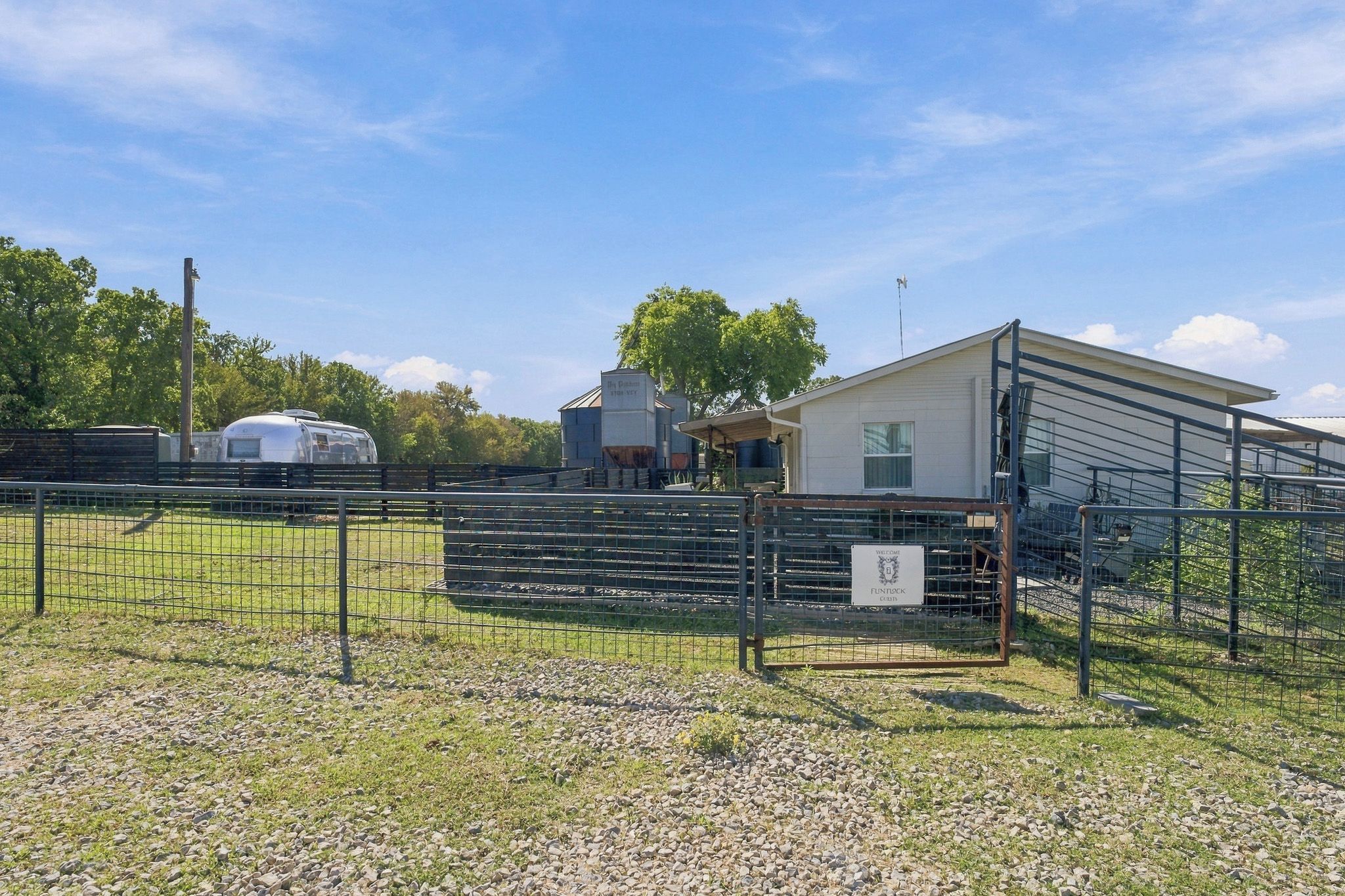 A fenced outdoor area with a trailer, a building with a sign, and a metal structure.