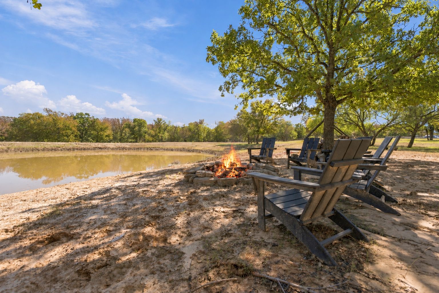 A lakeside setting with a campfire and wooden chairs.