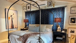 Ein Schlafzimmer mit Himmelbett, Baldachin, Nachttisch, Lampe und einer an der Wand montierten Ablagefläche.