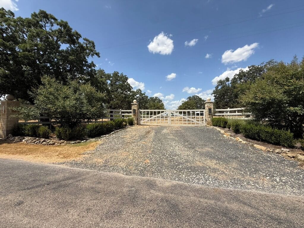 A gated driveway leading to a building with a stone wall on one side and a metal gate.
