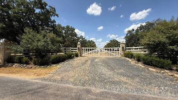 A gated driveway leading to a building with a stone wall on one side and a metal gate.