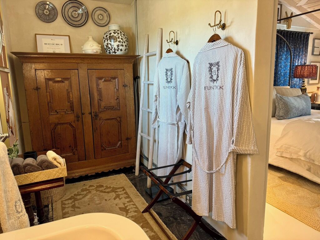 Ein Hotelzimmer mit einem Holzschrank, einem Kleiderständer mit gestreiften Bademänteln und einem Bett mit blauer Vorhang.