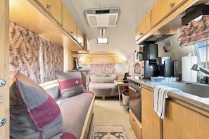 A compact RV interior with a kitchenette, a sofa, and a small table.