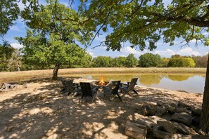 A campsite with a fire pit surrounded by chairs, a pond, and trees.