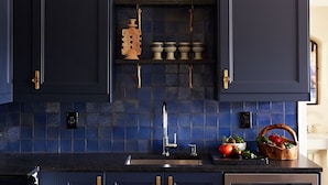 A kitchen with dark blue cabinets, a tiled backsplash, and a sink.