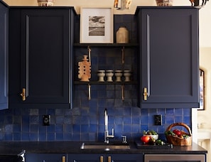 A kitchen with dark blue cabinets, a tiled backsplash, and a sink.
