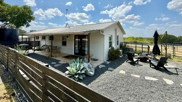 Ein modernes Haus mit einer Terrassenfläche, Sitzgelegenheiten im Freien und Blick auf die Landschaft.