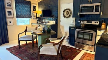 A modern kitchen with dark blue cabinets, a stainless steel stove, and a microwave. There is a dining area with two chairs and a table.