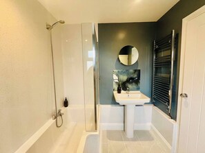 Un bagno moderno con doccia vetro, lavabo su piedistallo e uno specchio grande.