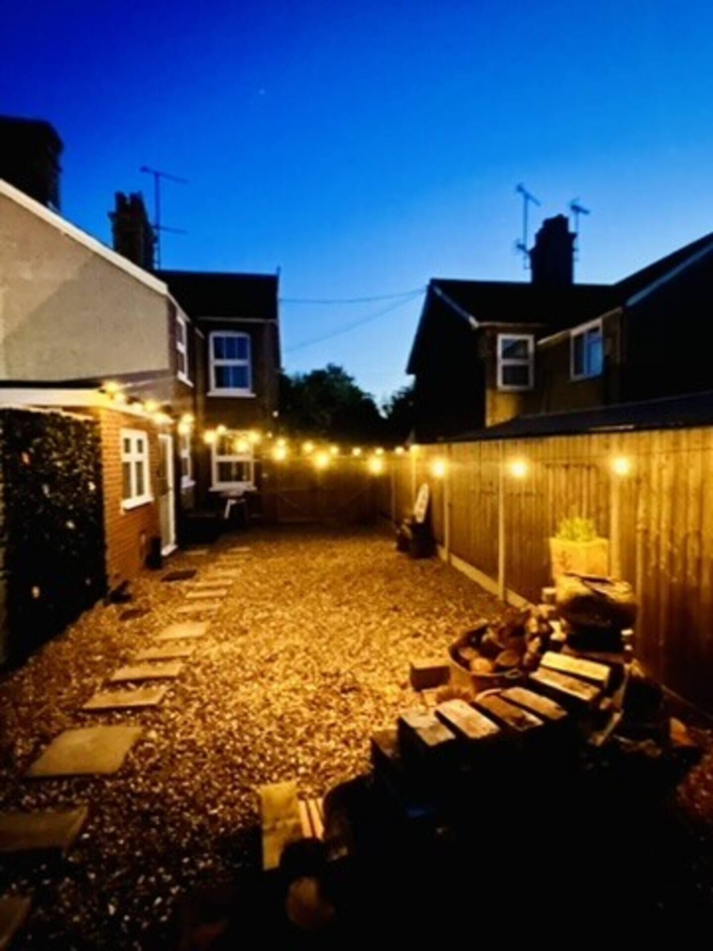 A backyard with a gravel surface, a wooden fence, and string lights.