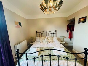 Quarto com cama, radiador, luminária e cabides.