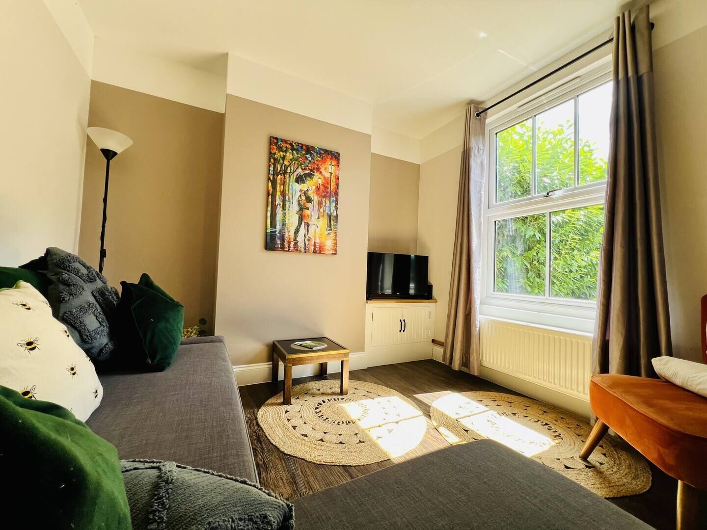 Uma sala de estar com sofá, mesinha, televisão e janela com cortinas.