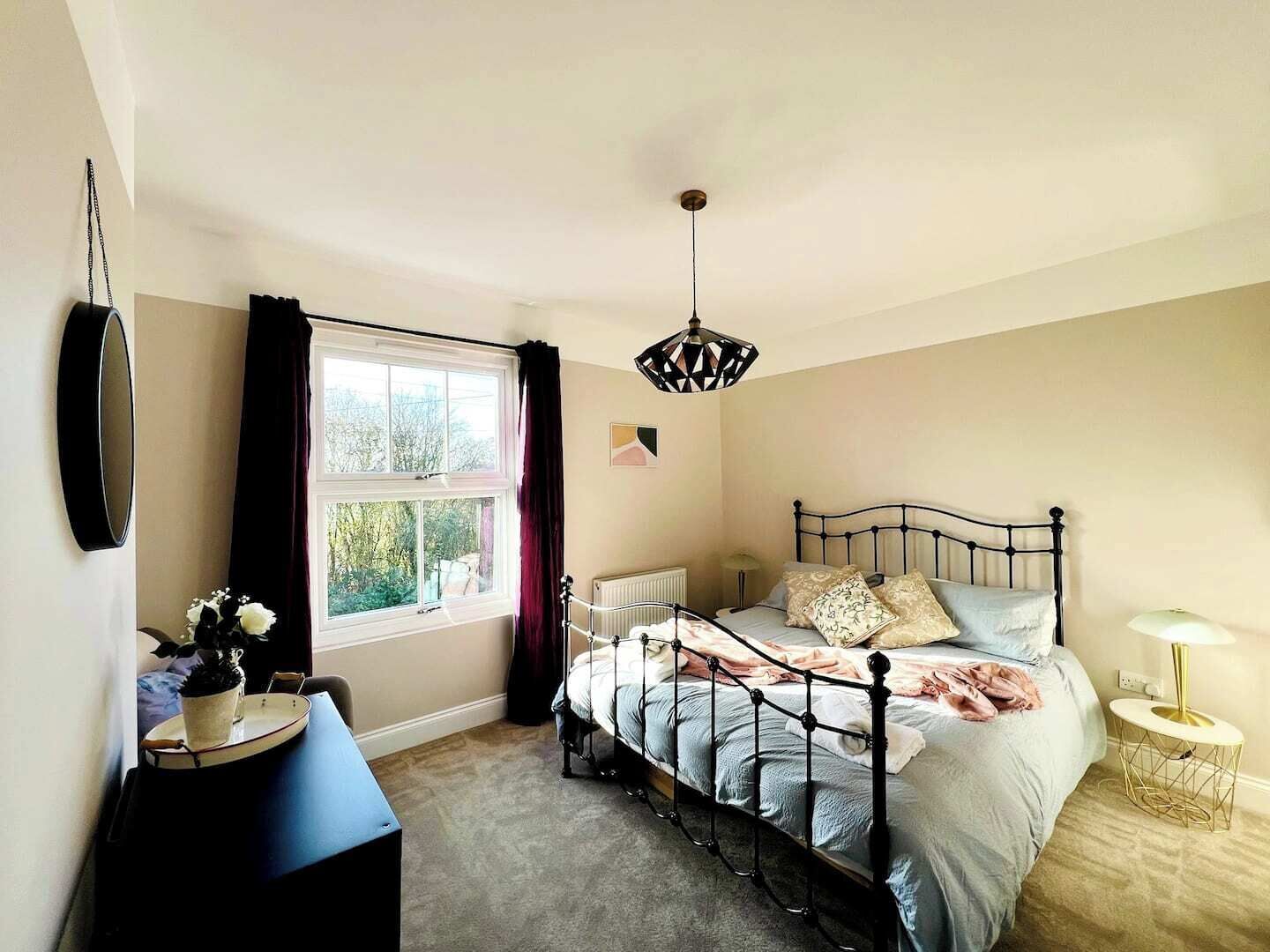 Een slaapkamer met een bed, nachtkastje, lamp, raam en gordijnen.