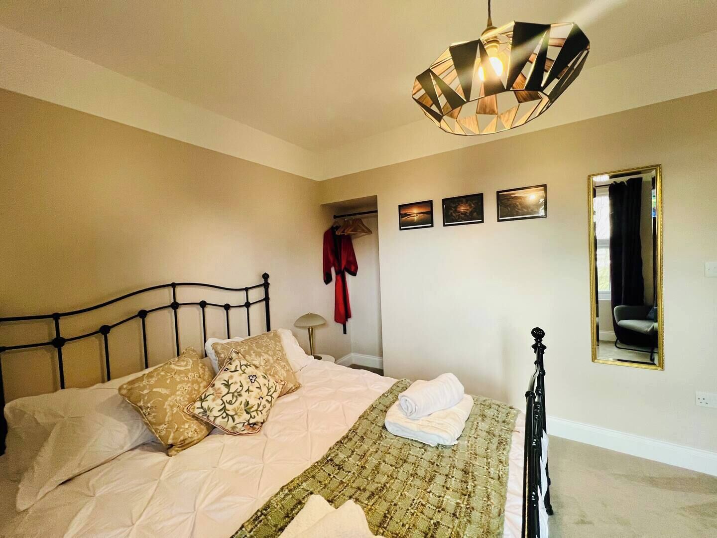 Een slaapkamer met een bed, een hanglamp, een spiegel en een muur met drie foto's.