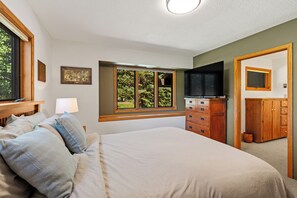 A bedroom with a bed, a dresser, a television, and a window with a view of greenery. - Charming 5-bedroom house in wonderful Big Sky for your getaway (Big Sky)
