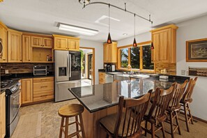 A modern kitchen with wooden cabinets, stainless steel appliances, and a large island with bar stools. - Charming 5-bedroom house in wonderful Big Sky for your getaway (Big Sky)