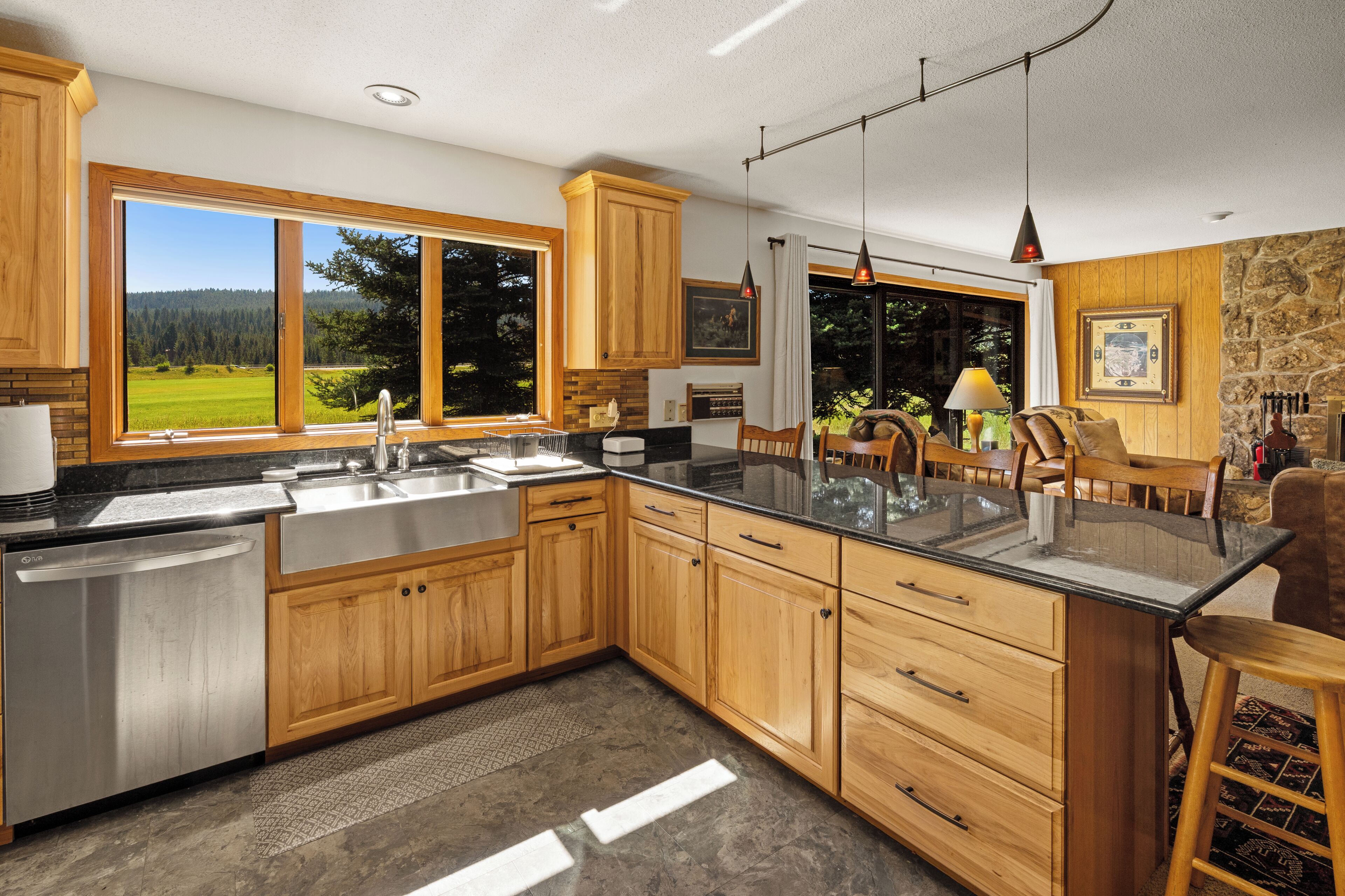 A modern kitchen with wooden cabinets, a stainless steel sink, and a large window overlooking a green landscape.