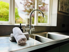 A kitchen with a stainless steel sink, a towel, and a window with a view of greenery. - Boutique Home & Private Garden | City Escape (Colchester)