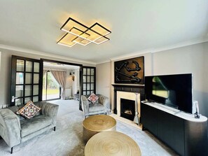 A modern living room with a fireplace, a television, and a large window. - Boutique Home & Private Garden | City Escape (Colchester)