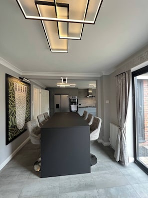 A modern dining area with a central table, chairs, and a kitchen in the background. - Boutique Home & Private Garden | City Escape (Colchester)