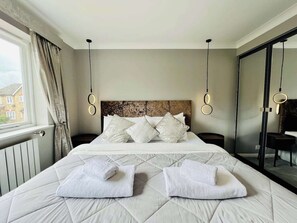A hotel room with a large bed, two bedside tables, a headboard, and a view of the outside. - Boutique Home & Private Garden | City Escape (Colchester)