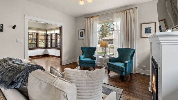 Une pièce avec une cheminée, deux fauteuils, un canapé et une fenêtre avec des rideaux.
