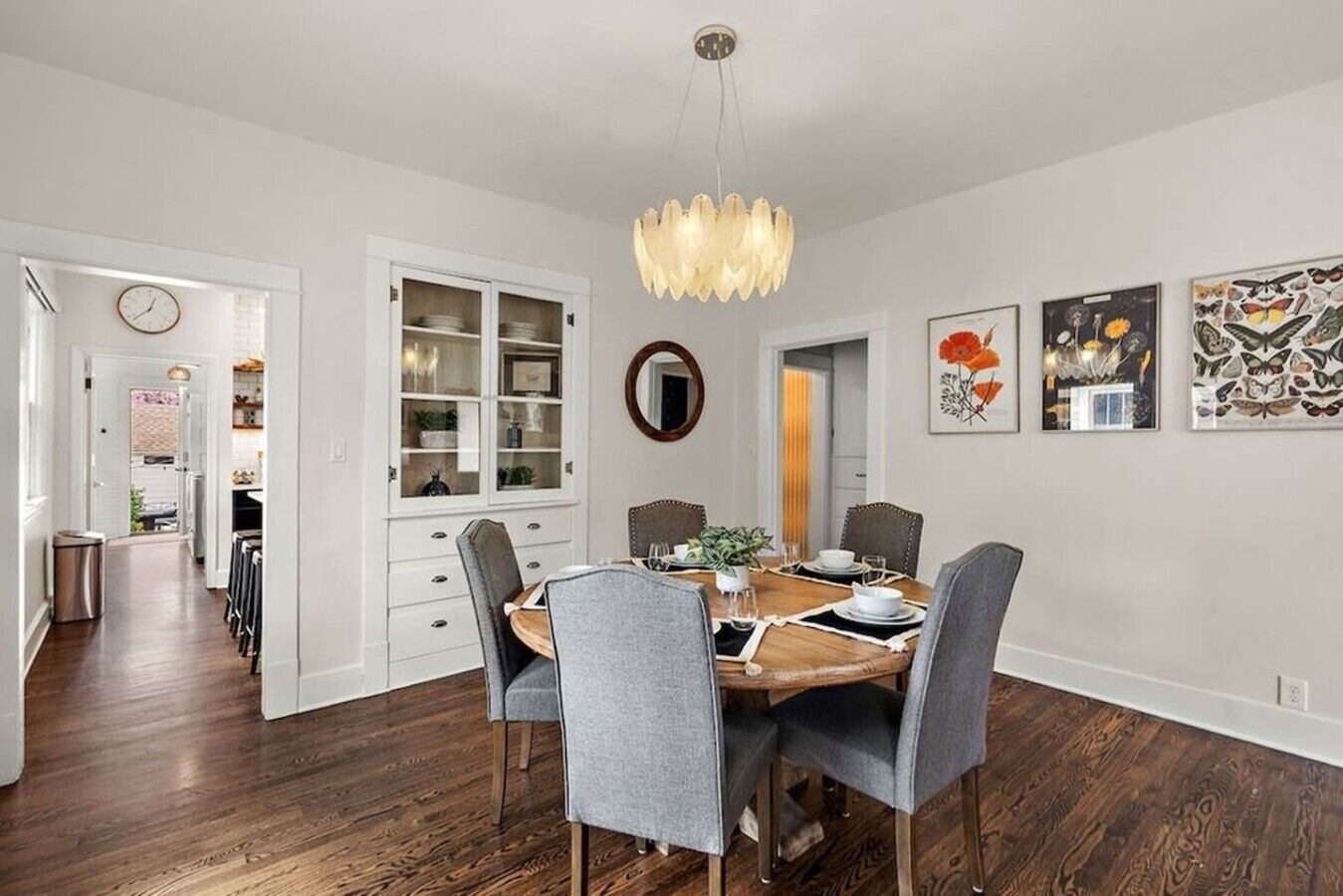 Un'area pranzo con tavolo in legno, sedie grigie, un lampadario e decorazioni a parete.