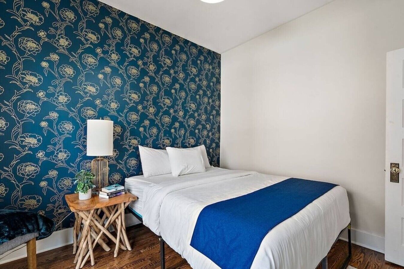 A bedroom with a bed, bedside table, lamp, and a blue floral wallpaper.