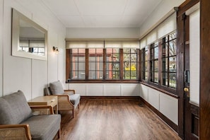 Une pièce dotée d’une grande baie vitrée, d’un plancher en bois et d’un coin salon avec un canapé et des fauteuils.