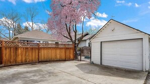 Un garage attenant à une maison, avec une clôture en bois et un cerisier en fleurs.