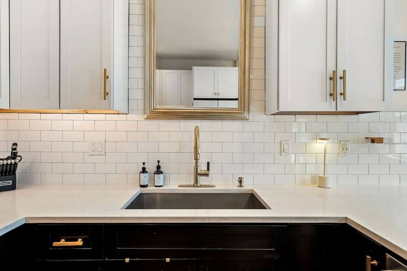 Una cucina moderna con mobili bianchi, un lavello in acciaio inossidabile e un grande specchio sopra il piano di lavoro.