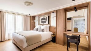 Quarto de hotel com uma cama grande, uma escrivaninha, uma cadeira, um espelho e uma janela com cortinas.