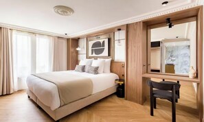 Una habitación de hotel con una cama grande, un escritorio, una silla, un espejo y un ventanal con cortinas.