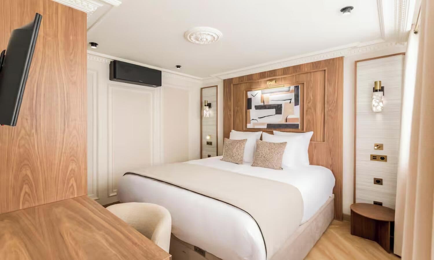 Una habitación de hotel con cama, escritorio, silla, televisor y espejo.
