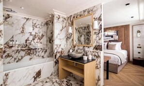 Un baño con pared de mármol, una bañera, un lavabo y un espejo.