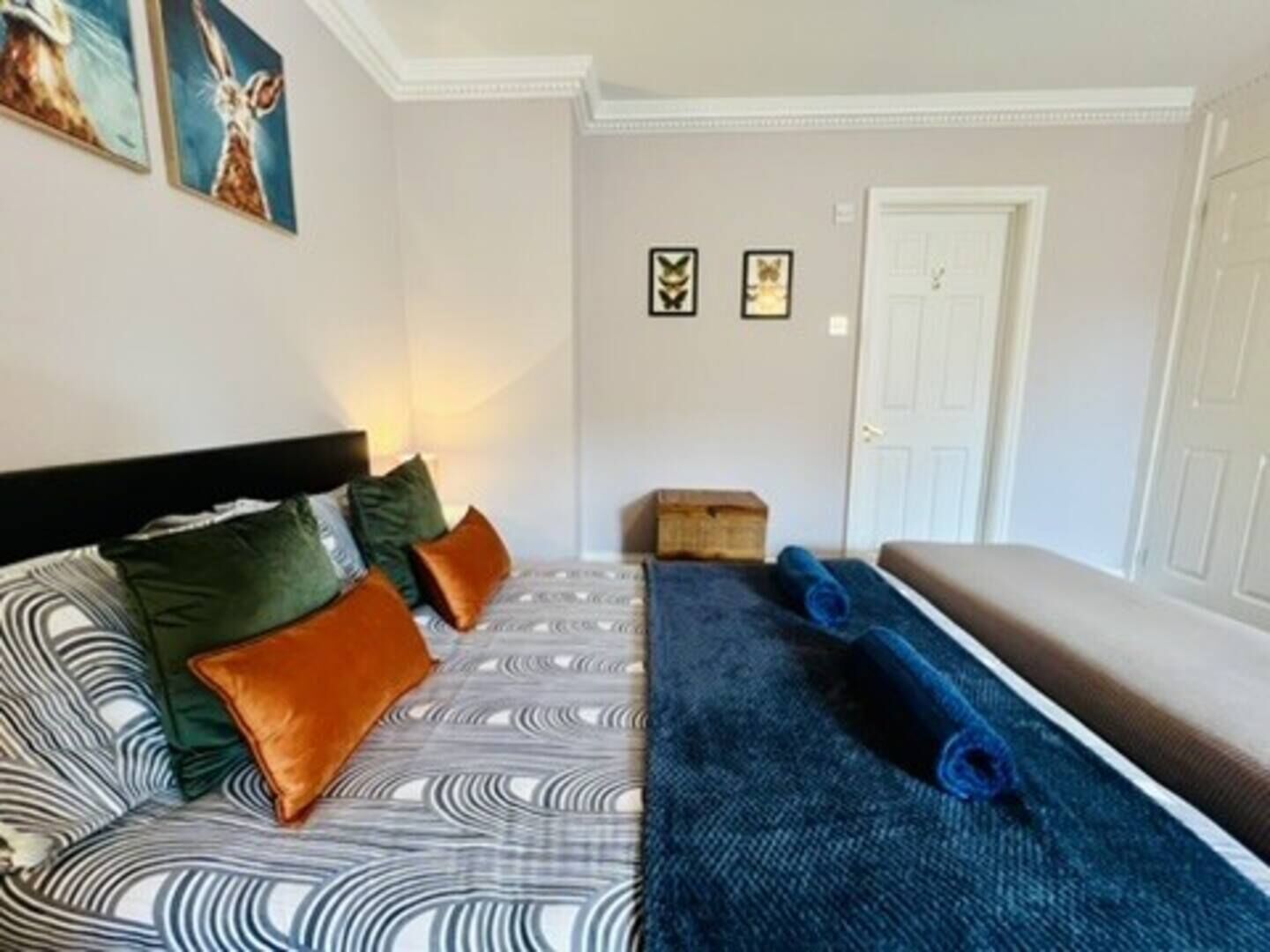 A bedroom with a bed, pillows, a blue blanket, a bench, and framed pictures on the wall.