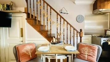 A dining area with a wooden staircase, a clock on the wall, and a kitchen in the background.