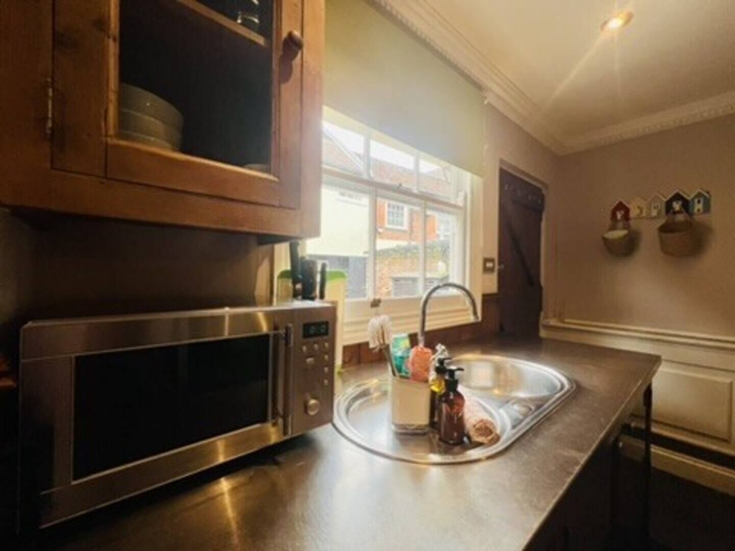 A kitchen with a stainless steel microwave, a sink with a faucet, and a window with a view of buildings outside.