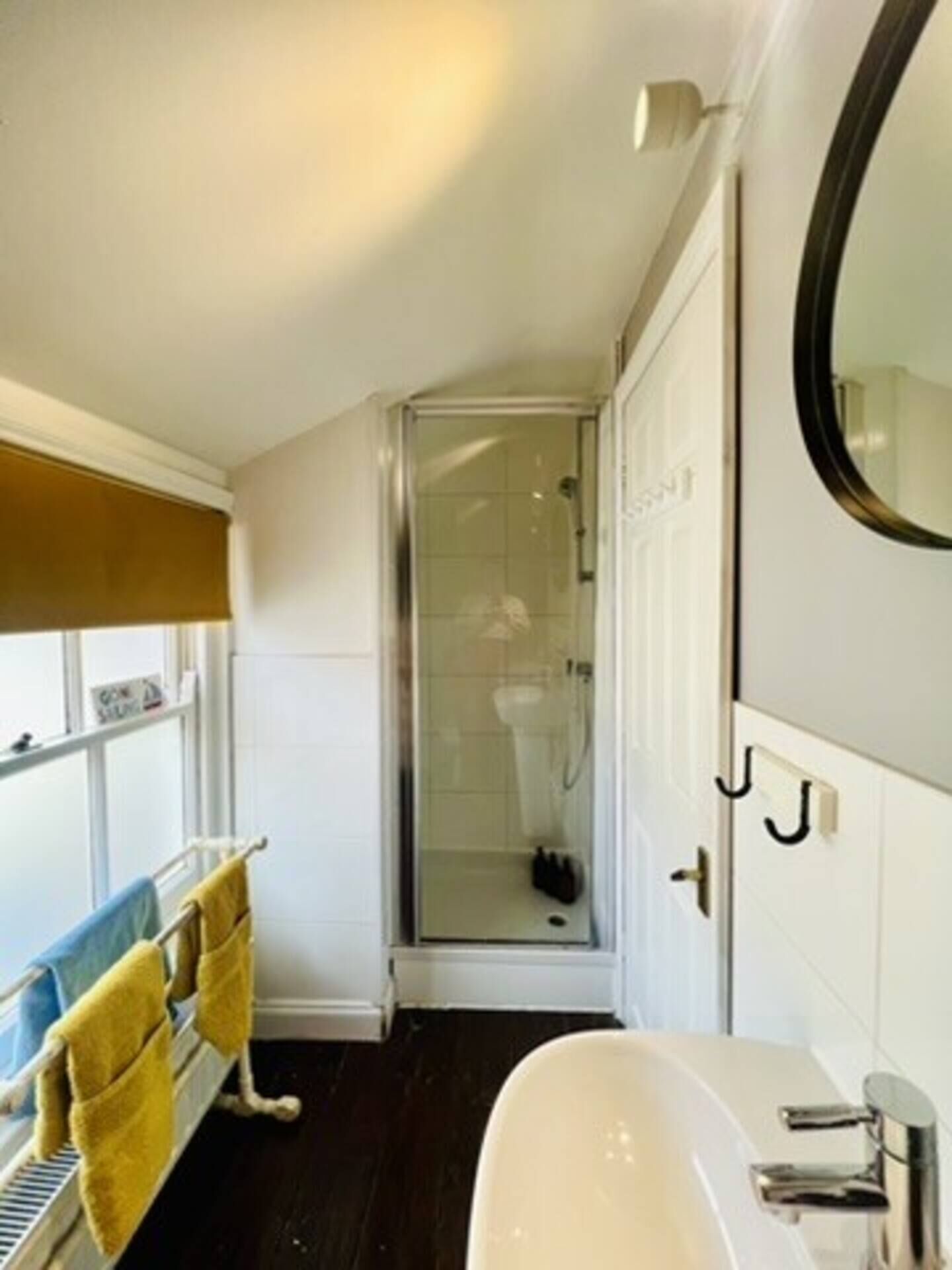 A bathroom with a white sink, a glass shower enclosure, and a towel rack with yellow towels.