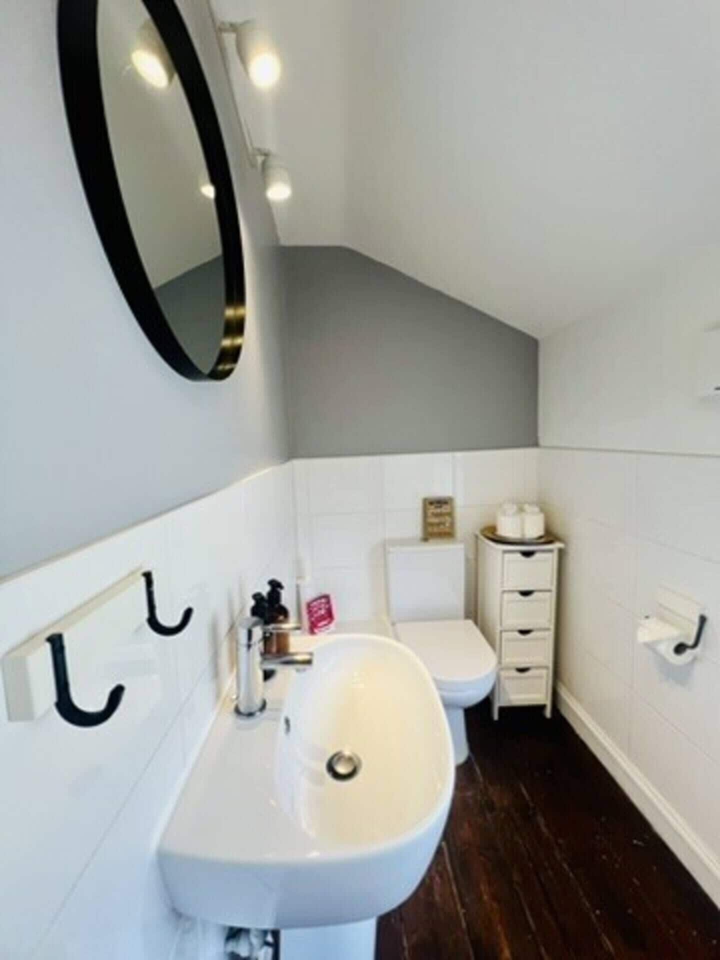 Een badkamer met een wit wastafel, een spiegel, een toilet en een klein kastje.