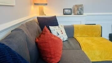 A living room with a grey sofa, colorful throw pillows, a yellow throw blanket, and a painting on the wall.